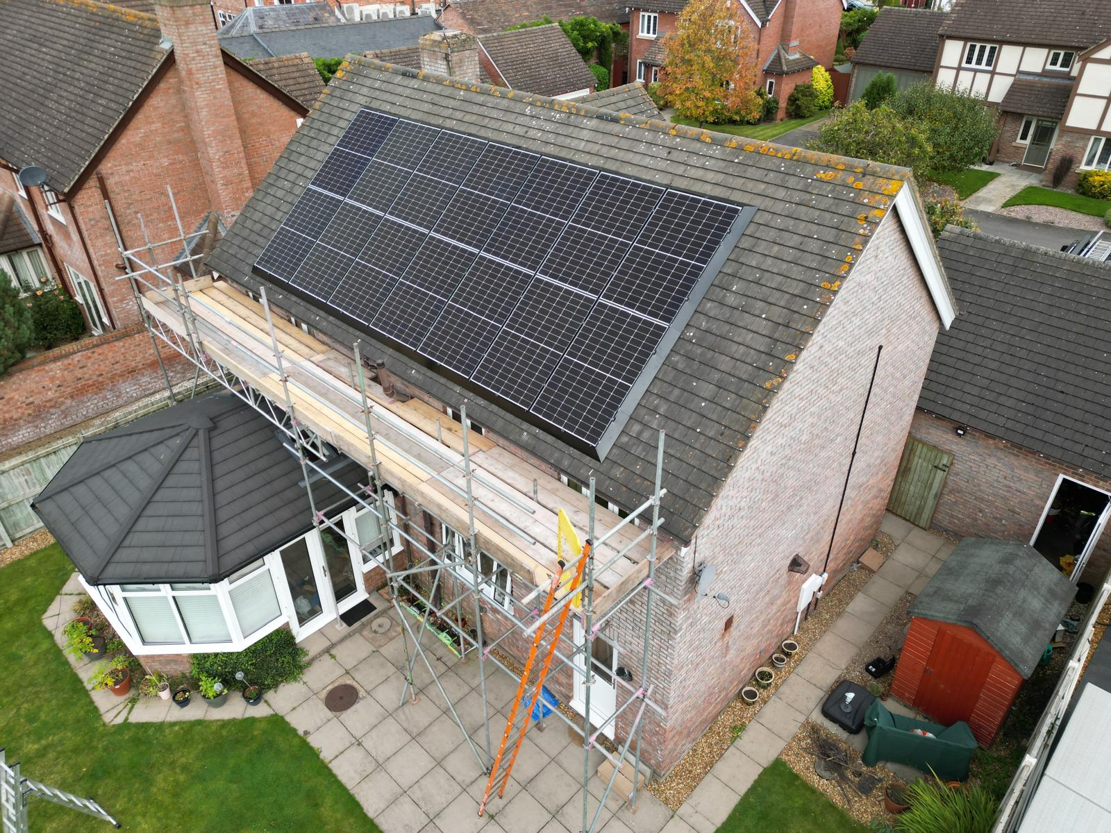 Residential house in West Midlands with rooftop solar panels under maintenance, scaffolding in place, conservatory and landscaped garden visible